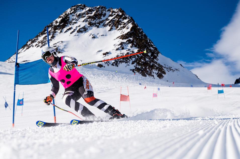 Ski-Fahrer in pinkem Wettkampfanzug fährt durch Torstangen auf einer verschneiten Piste mit Berg im Hintergrund.