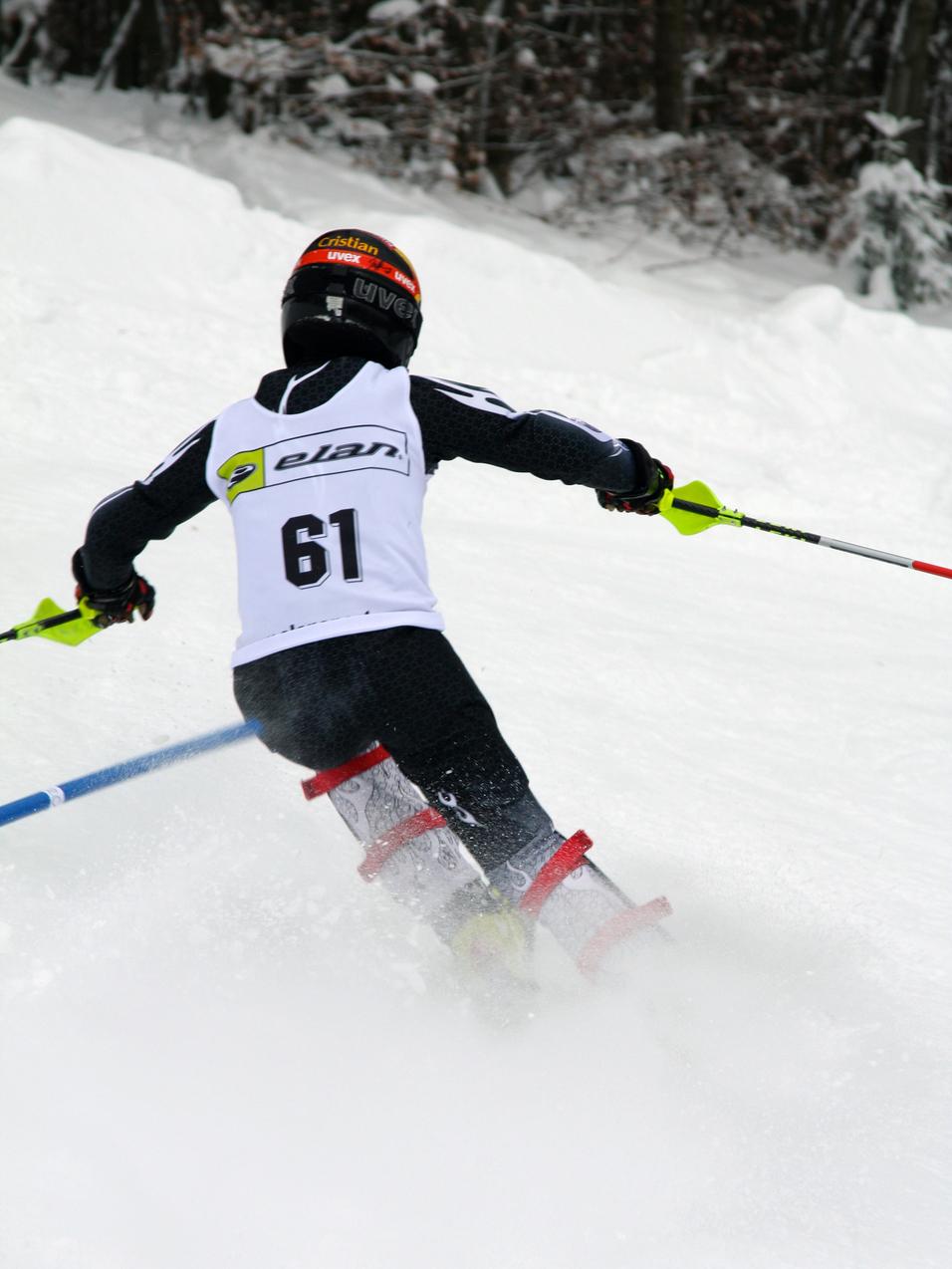 Skifahrer von hinten, der um ein Tor auf einer verschneiten Skipiste fährt, Wettkampfnummer 61 sichtbar.